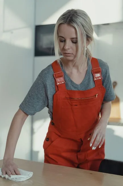 A woman in a gray sweater wipes a table with care, showcasing home cleaning in comfort.